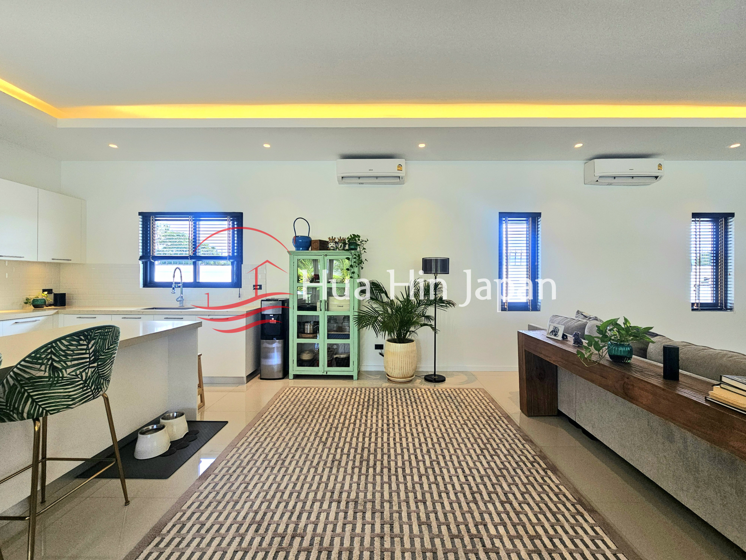 Bright open-plan kitchen and living area with a white island, patterned rug, indoor plants, and modern furnishings