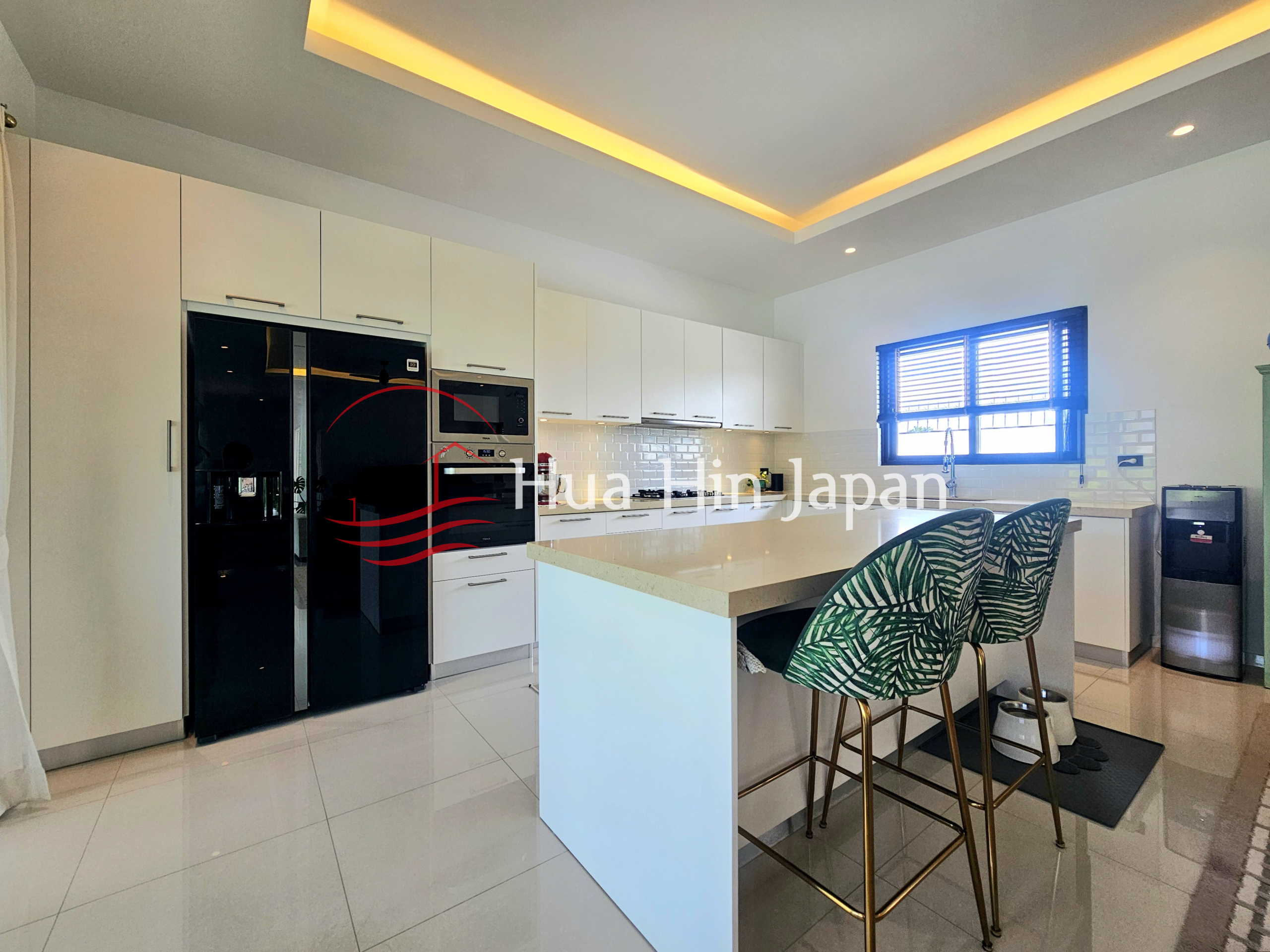 Modern white kitchen with a large island, built-in appliances, black refrigerator, and patterned bar stools