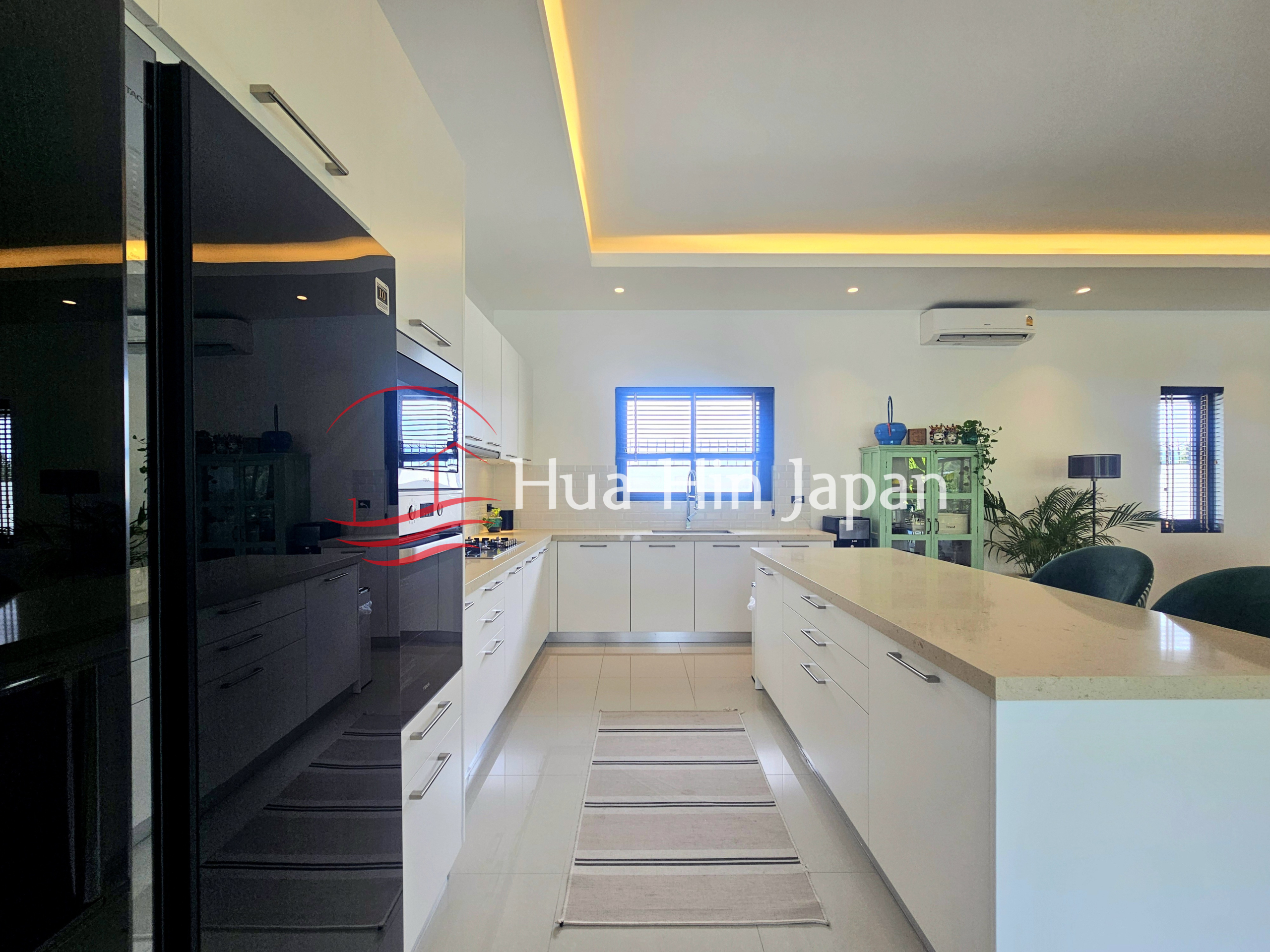Spacious modern kitchen with white cabinets, a large island, dark refrigerator, and warm recessed ceiling lighting