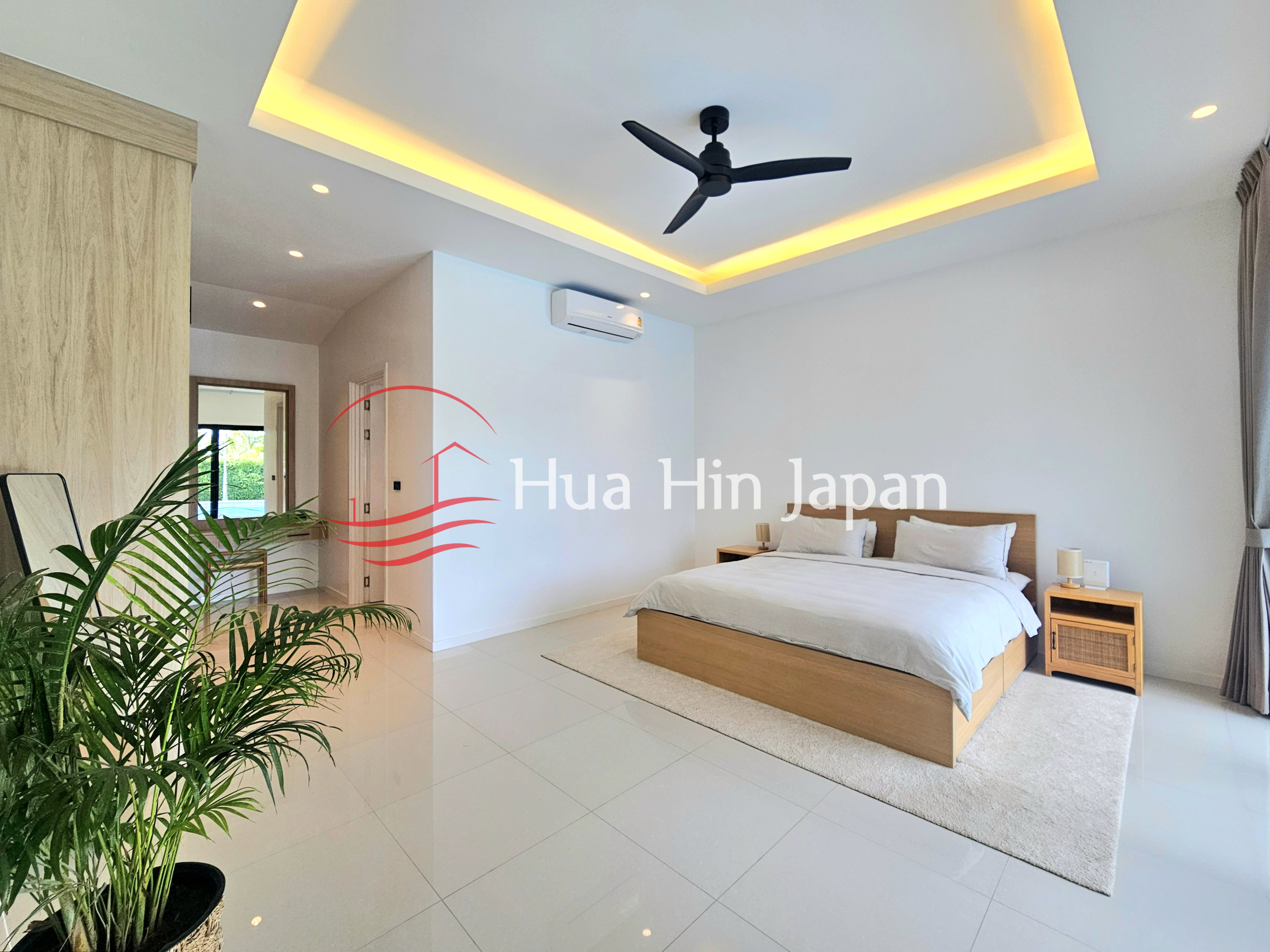 Spacious modern bedroom with a wooden bed, built-in wardrobe, ceiling fan, air conditioning, and indoor plants
