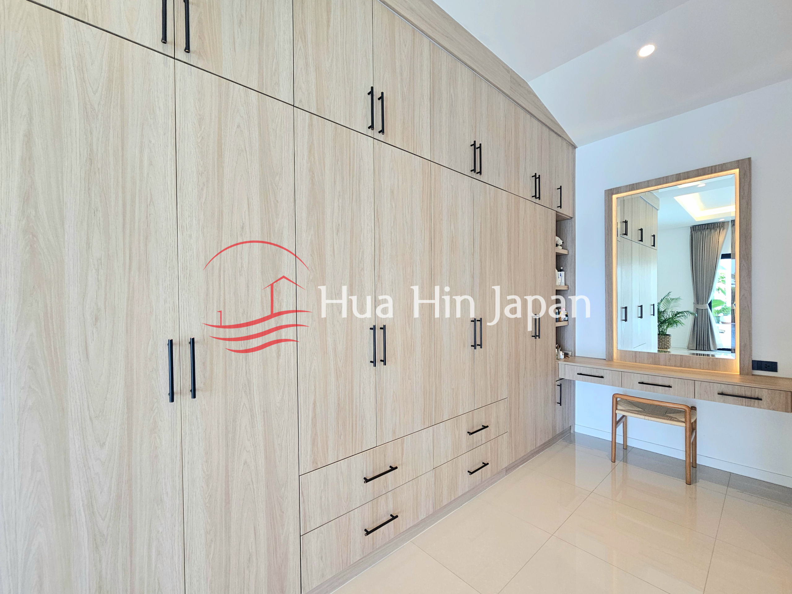 Spacious dressing room with built-in light wood wardrobes, drawers, and a large vanity mirror
