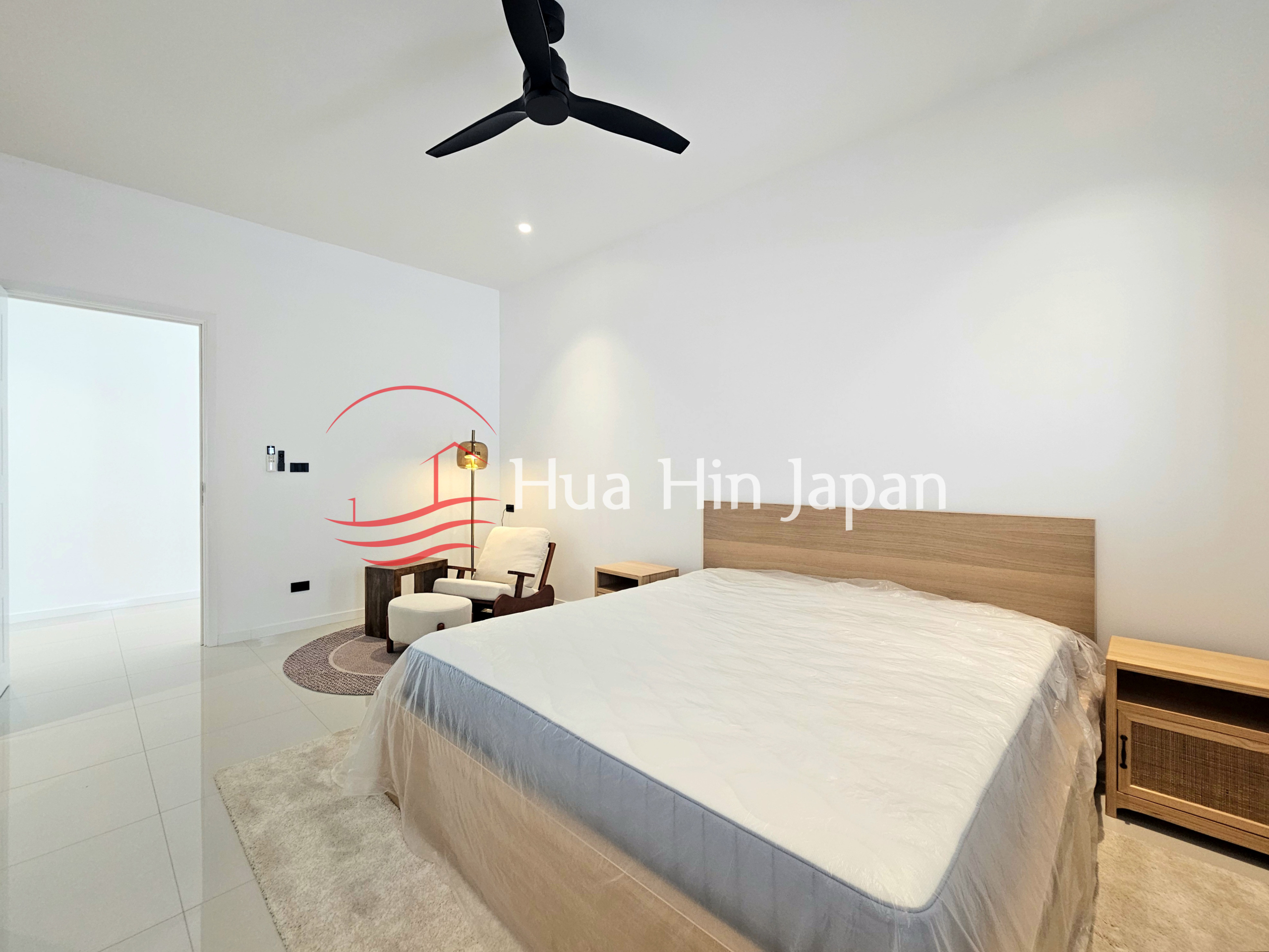 Bright modern bedroom with a large bed, wooden headboard, bedside tables, armchair, and ceiling fan