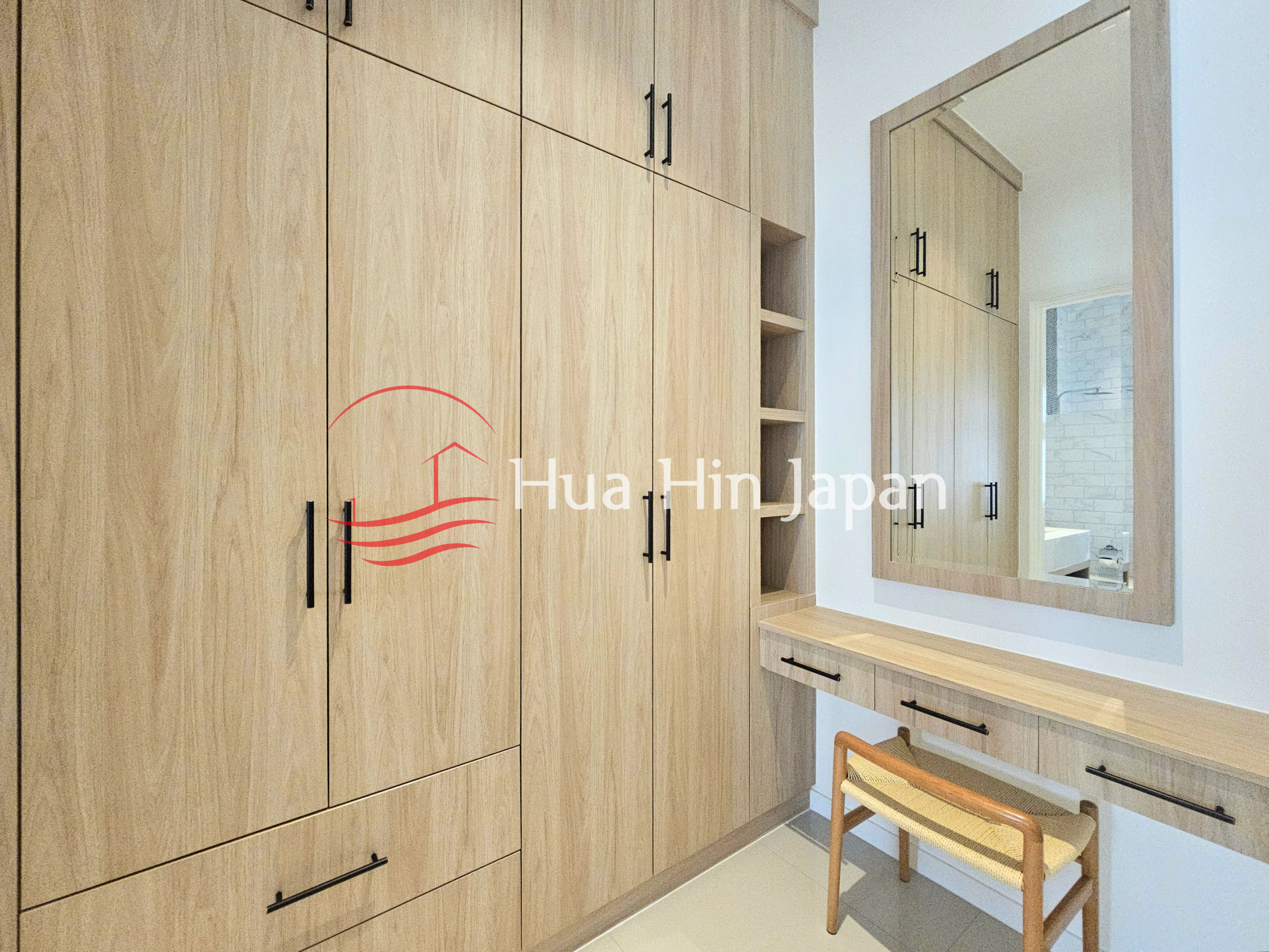 Modern dressing room with built-in light wood wardrobes, drawers, open shelving, large mirror, and vanity desk