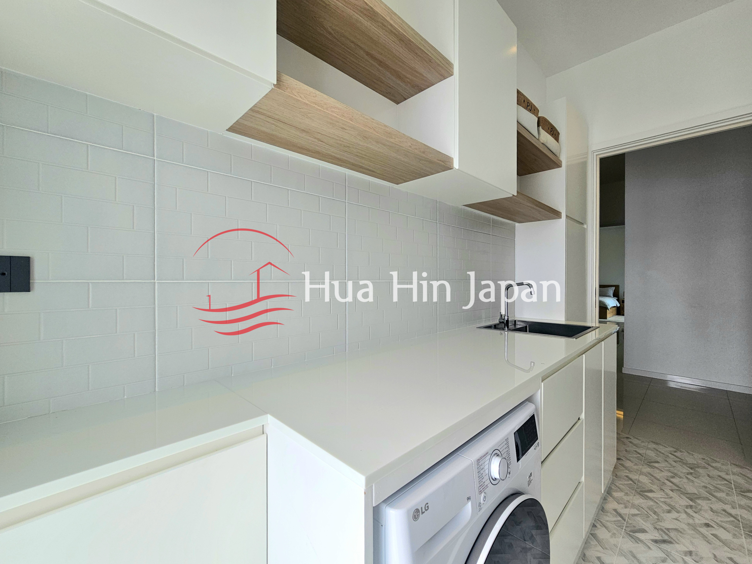 Modern white kitchen and laundry area with wooden open shelves, tiled backsplash, and an LG washing machine