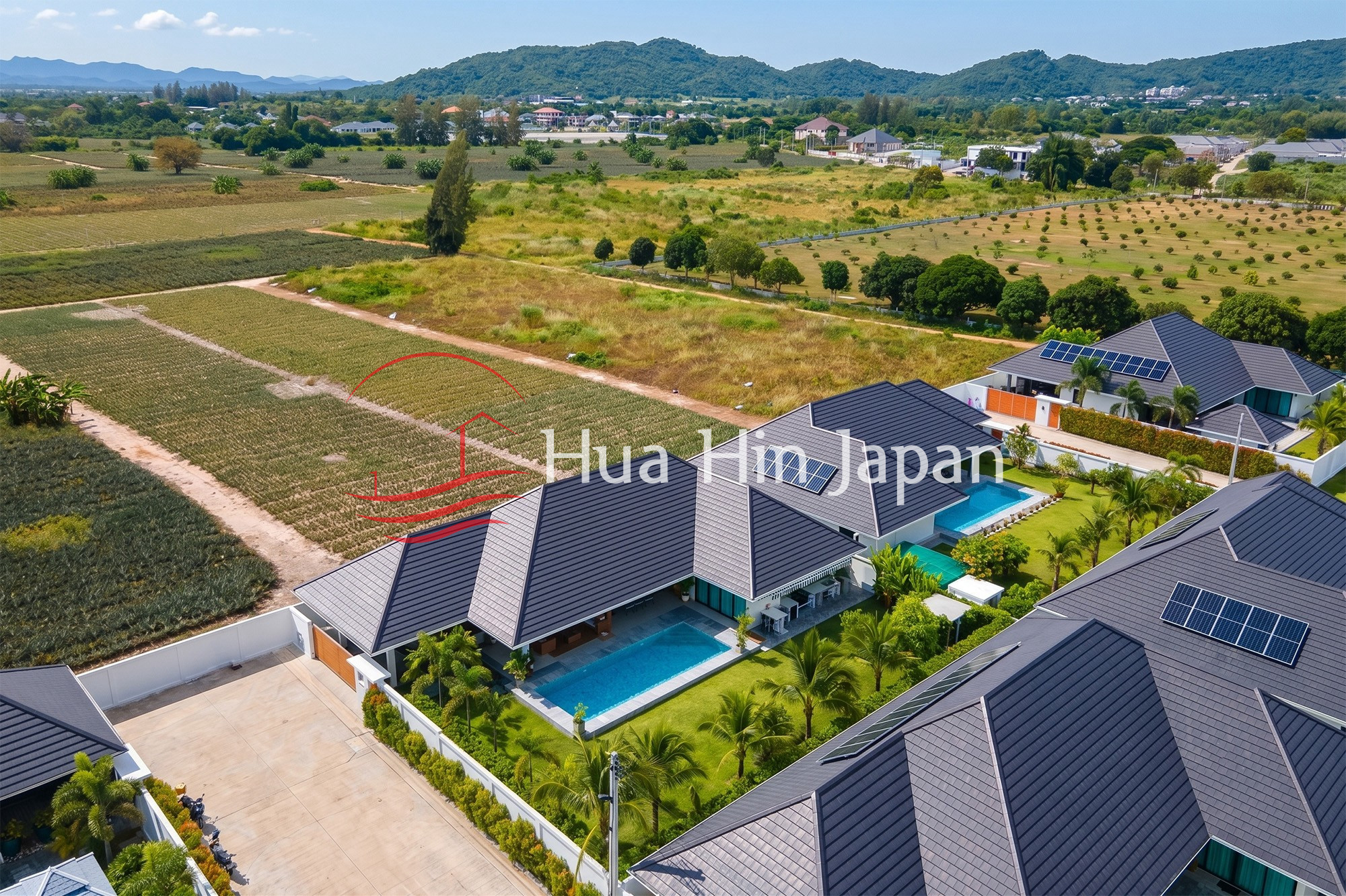 Aerial view of modern villas with private swimming pools surrounded by farmland and mountains