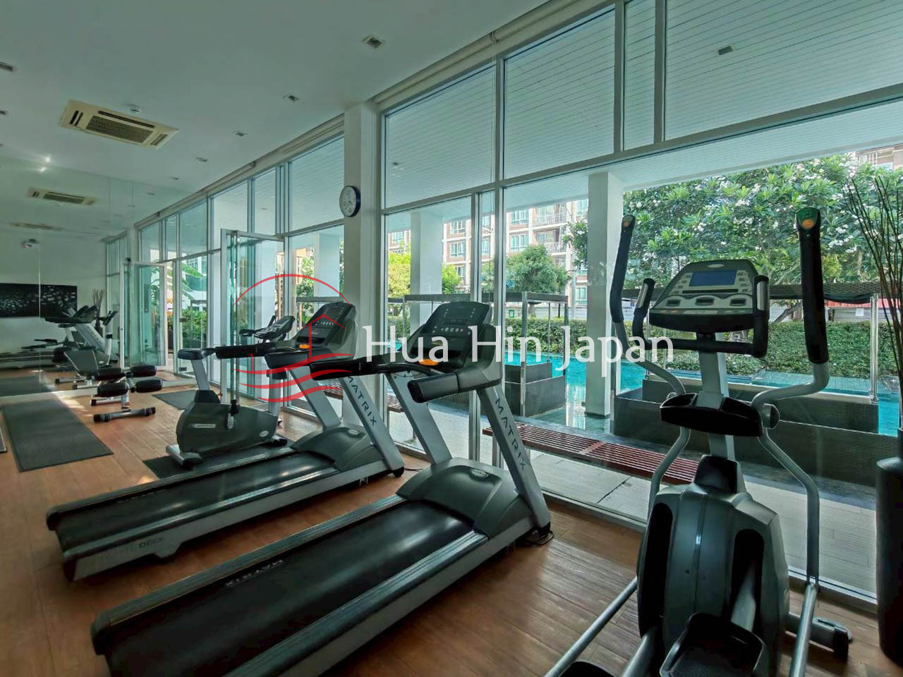 Modern condominium fitness room with treadmills, exercise bikes, large windows, and views of the pool