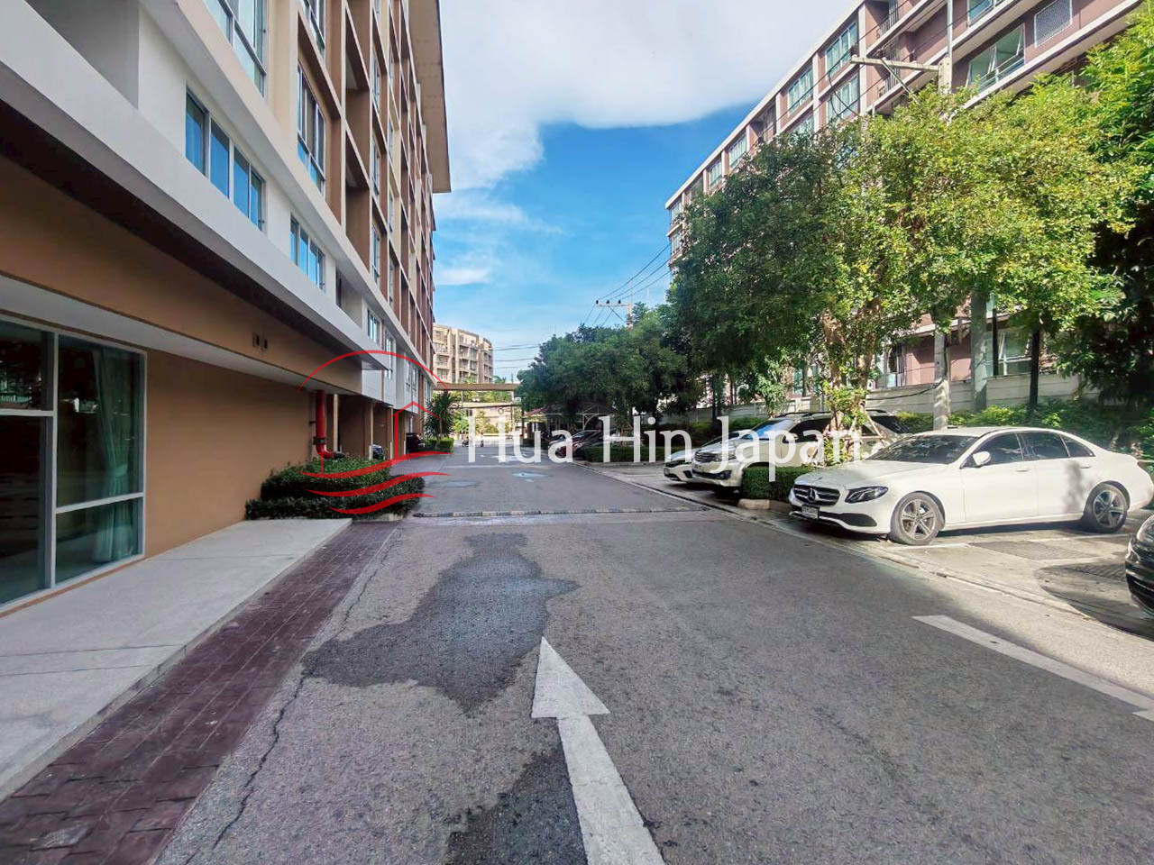 Residential condominium driveway with modern apartment buildings, parked cars, trees, and blue sky