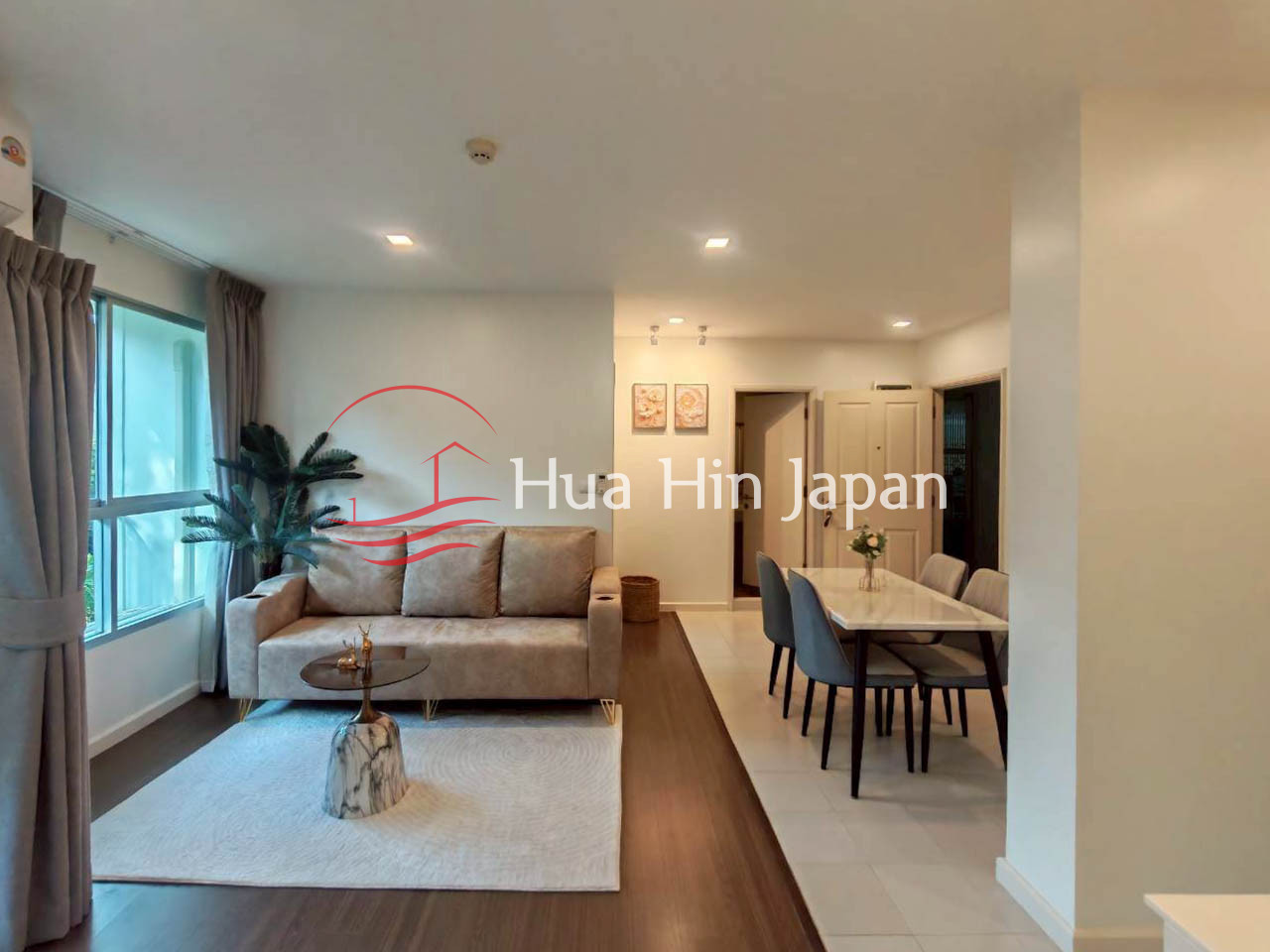 Modern apartment living room and dining area with a beige sofa, coffee table, large window, and six-seat dining table