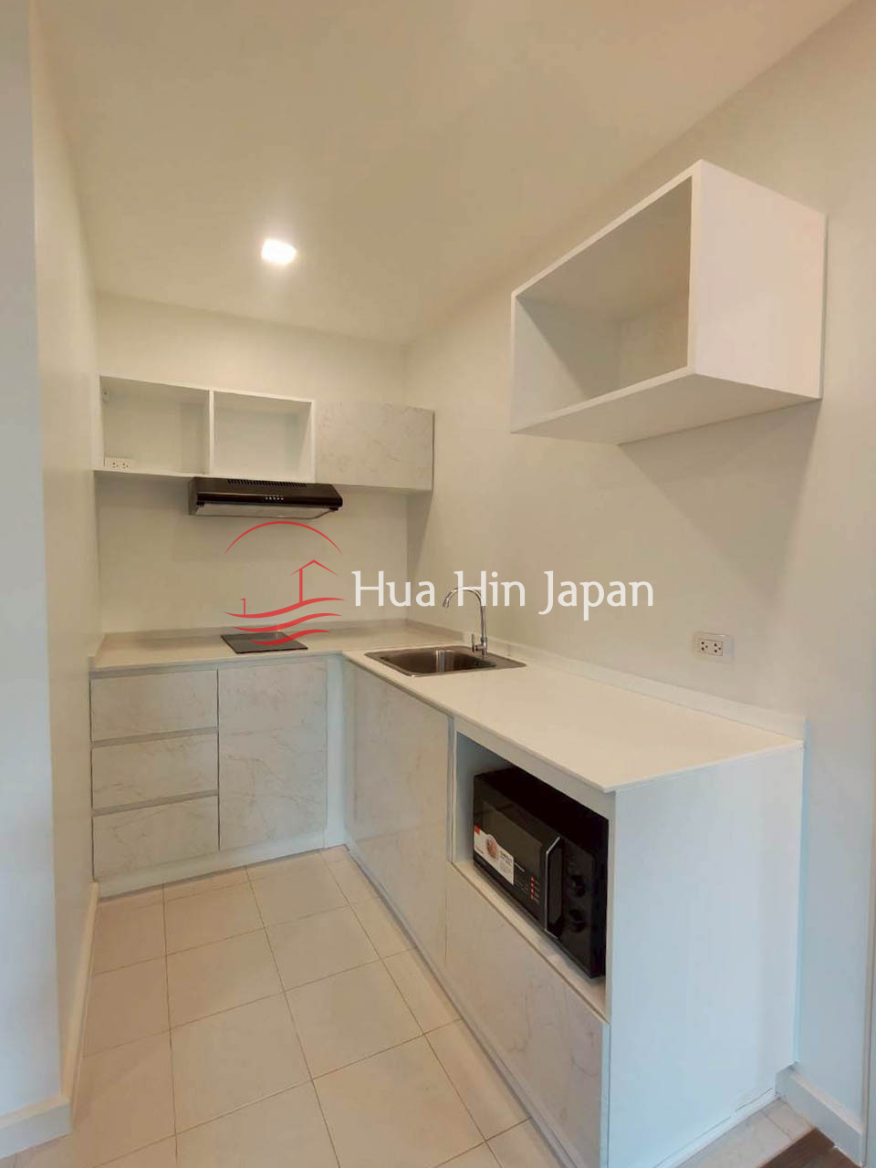 Compact modern kitchen with white cabinets, countertop, sink, induction cooktop, range hood, and built-in microwave