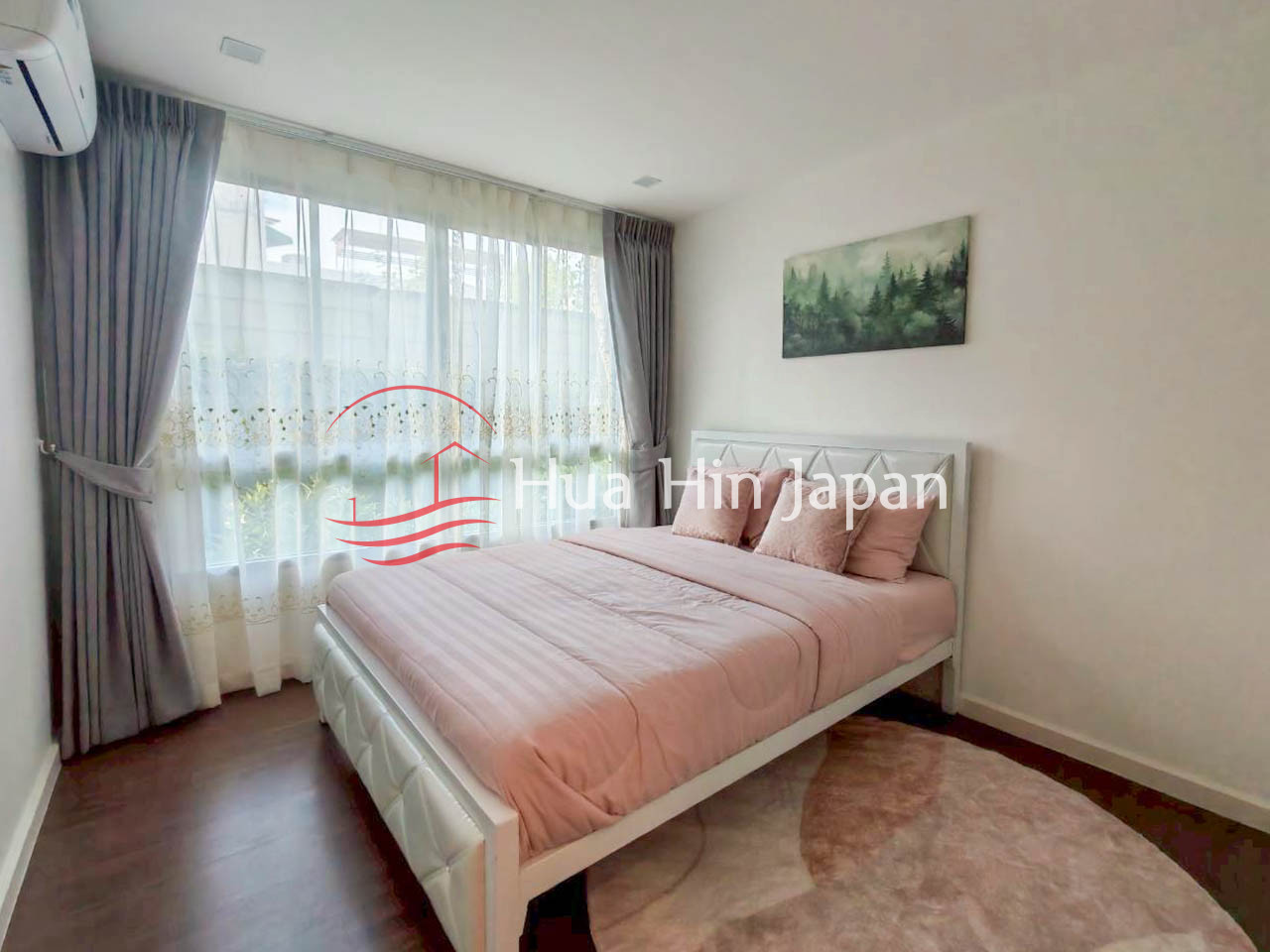 Bright bedroom with a white upholstered bed, soft pink bedding, large curtained window, and forest wall art
