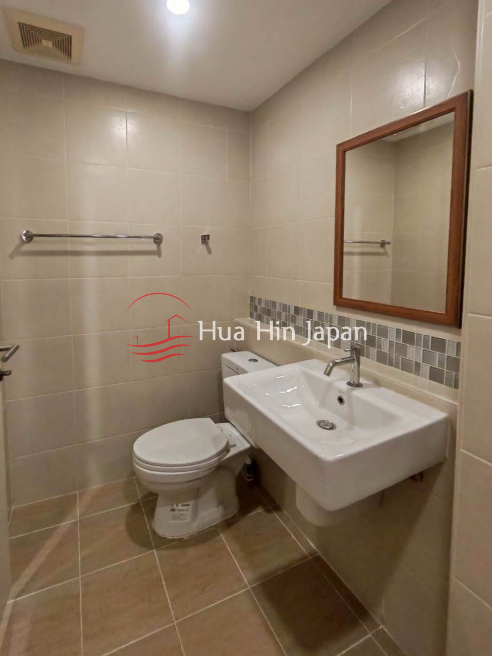 Compact modern bathroom with a white sink, toilet, wall mirror, and beige tiled walls
