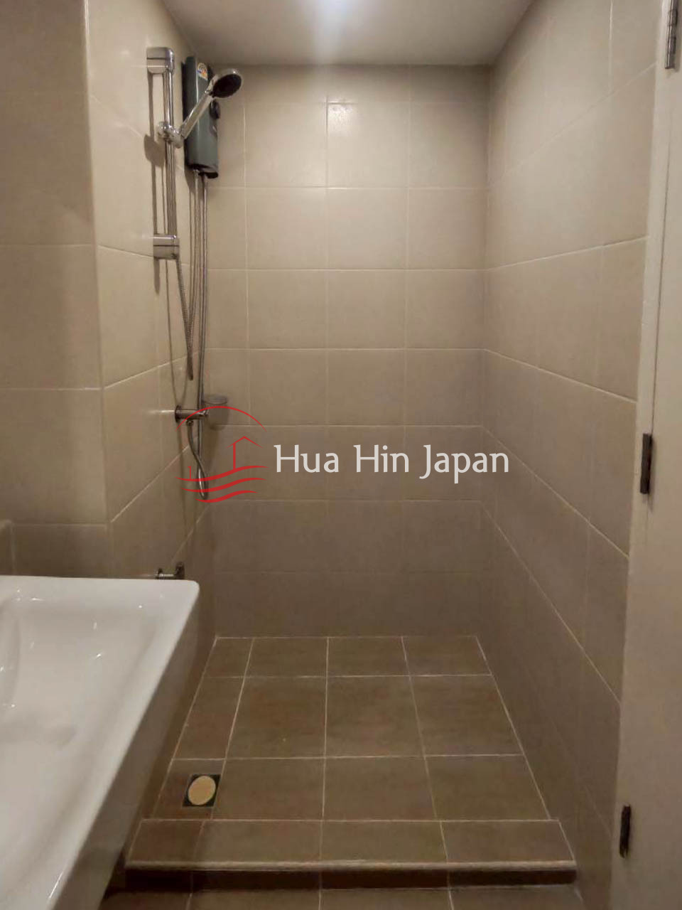Compact tiled bathroom shower area with a wall-mounted handheld shower and floor drain