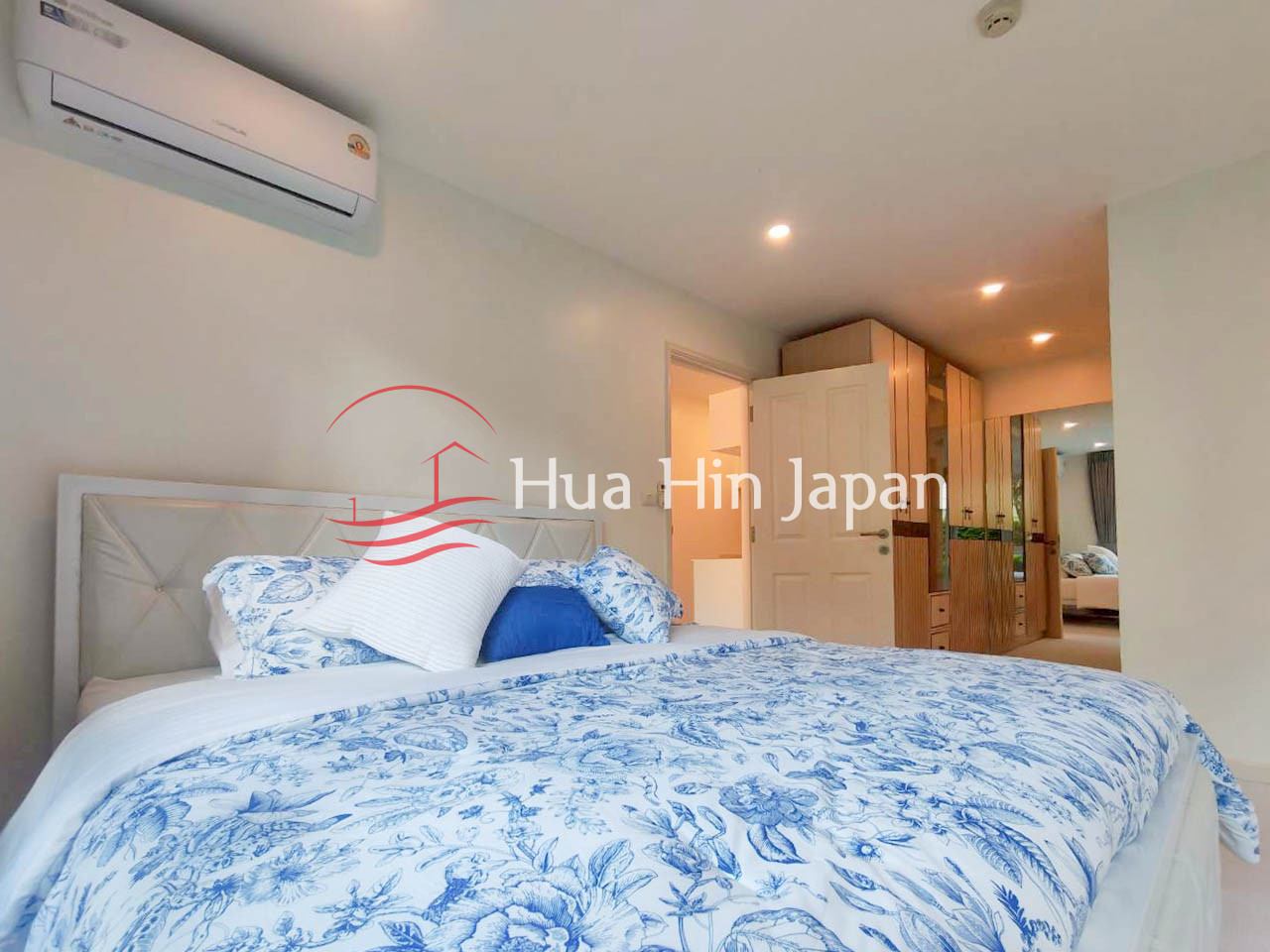 Bright modern bedroom with blue and white floral bedding, a large bed, air conditioner, and built-in wooden wardrobe