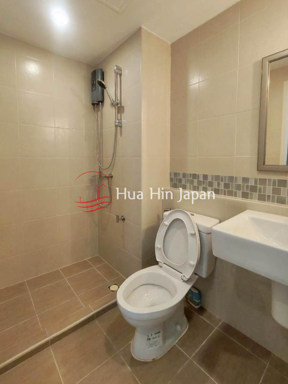 Modern bathroom with beige tiled walls, walk-in shower, toilet, and wall-mounted sink