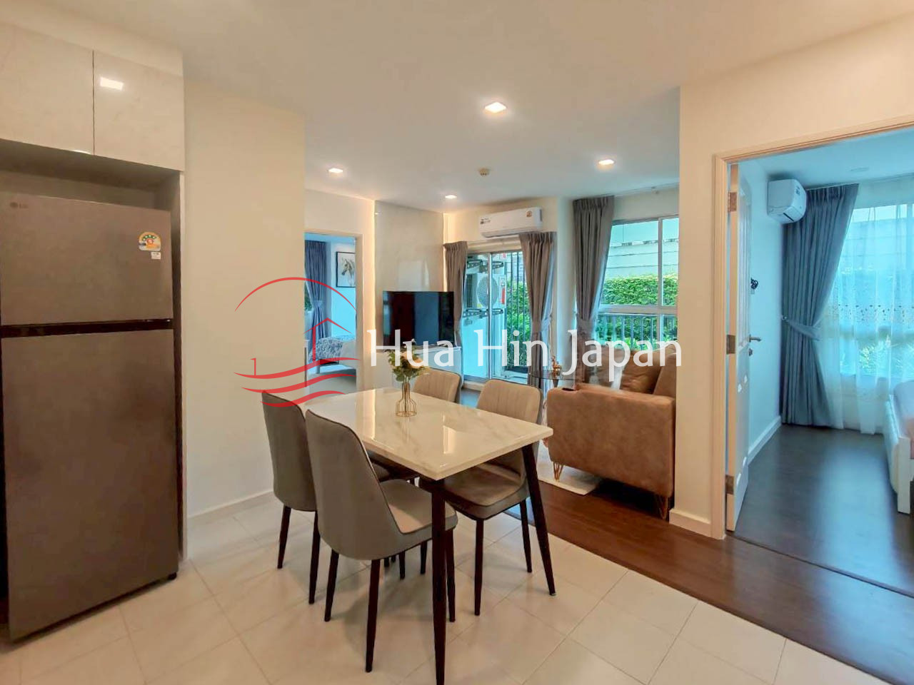 Modern apartment interior with a dining table, four chairs, living room, kitchen refrigerator, and adjoining bedroom