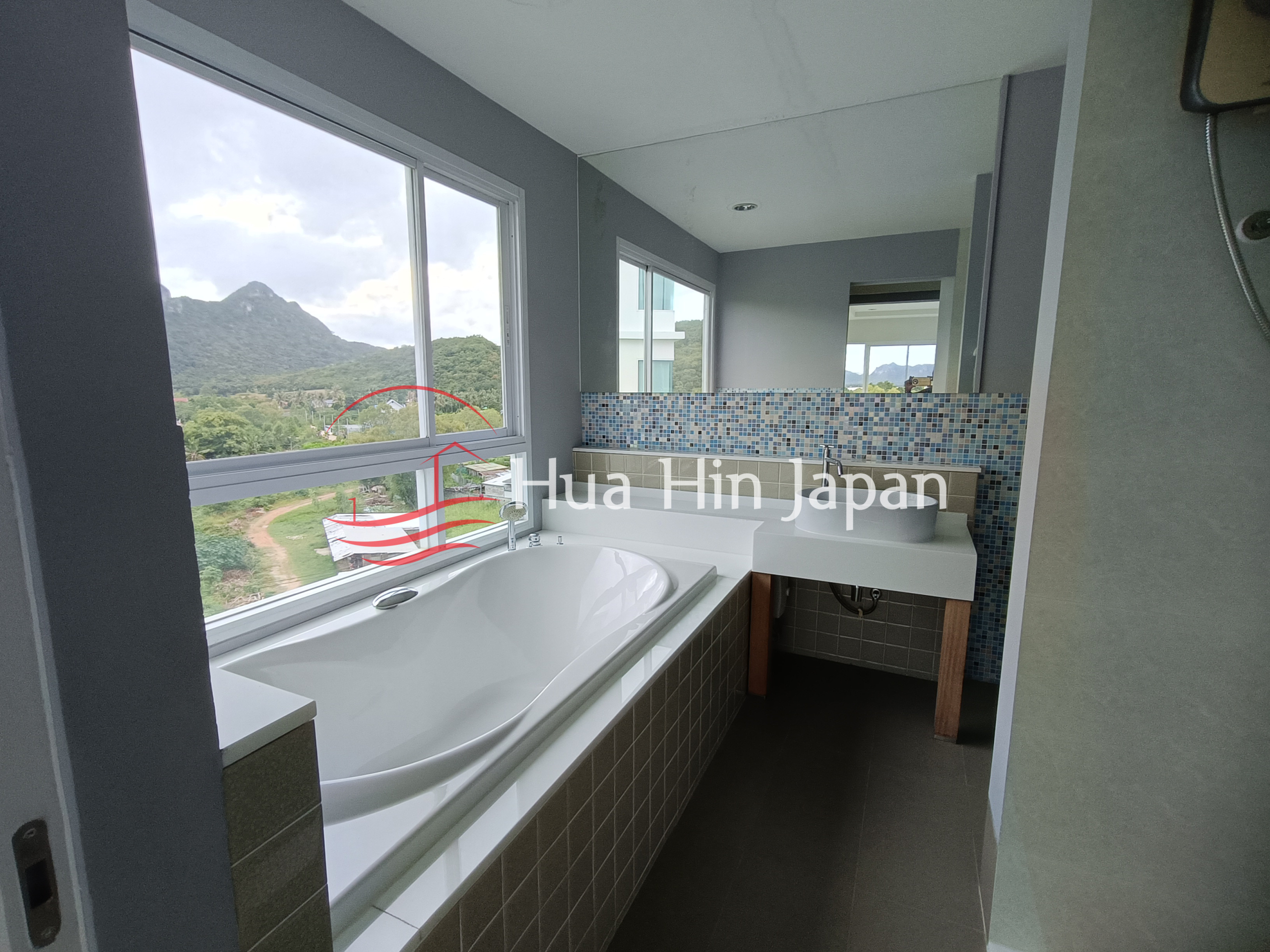 Modern bathroom with a bathtub, vanity, large mirror, and mountain view