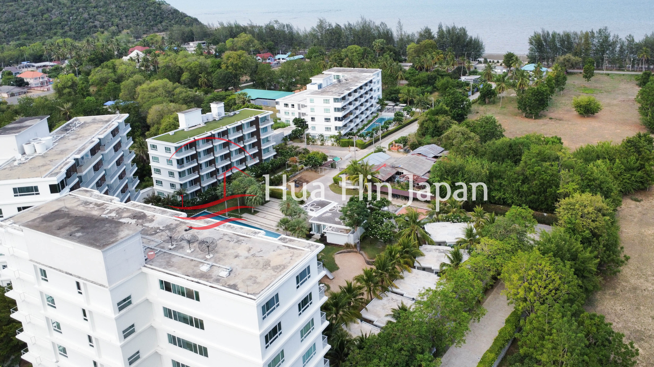 Aerial view of a modern condominium complex surrounded by tropical greenery near the beach