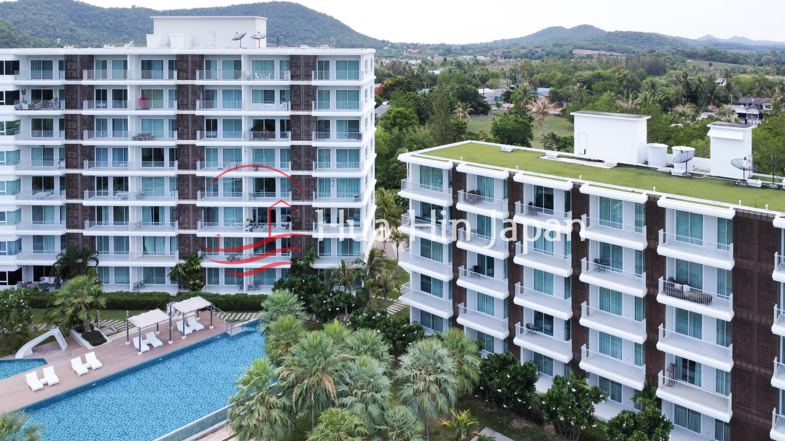 Modern luxury condominium buildings with a swimming pool, tropical landscaping, and mountain views