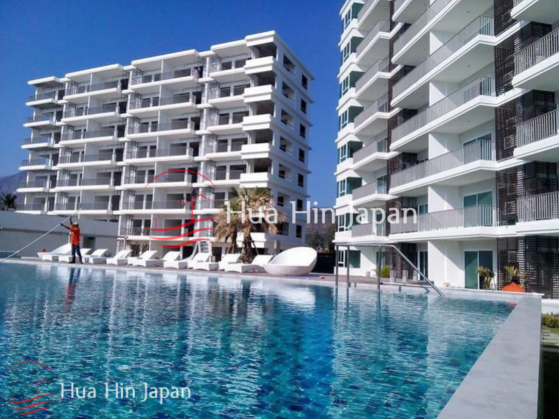 Modern white beachfront condominium buildings surrounding a large blue swimming pool