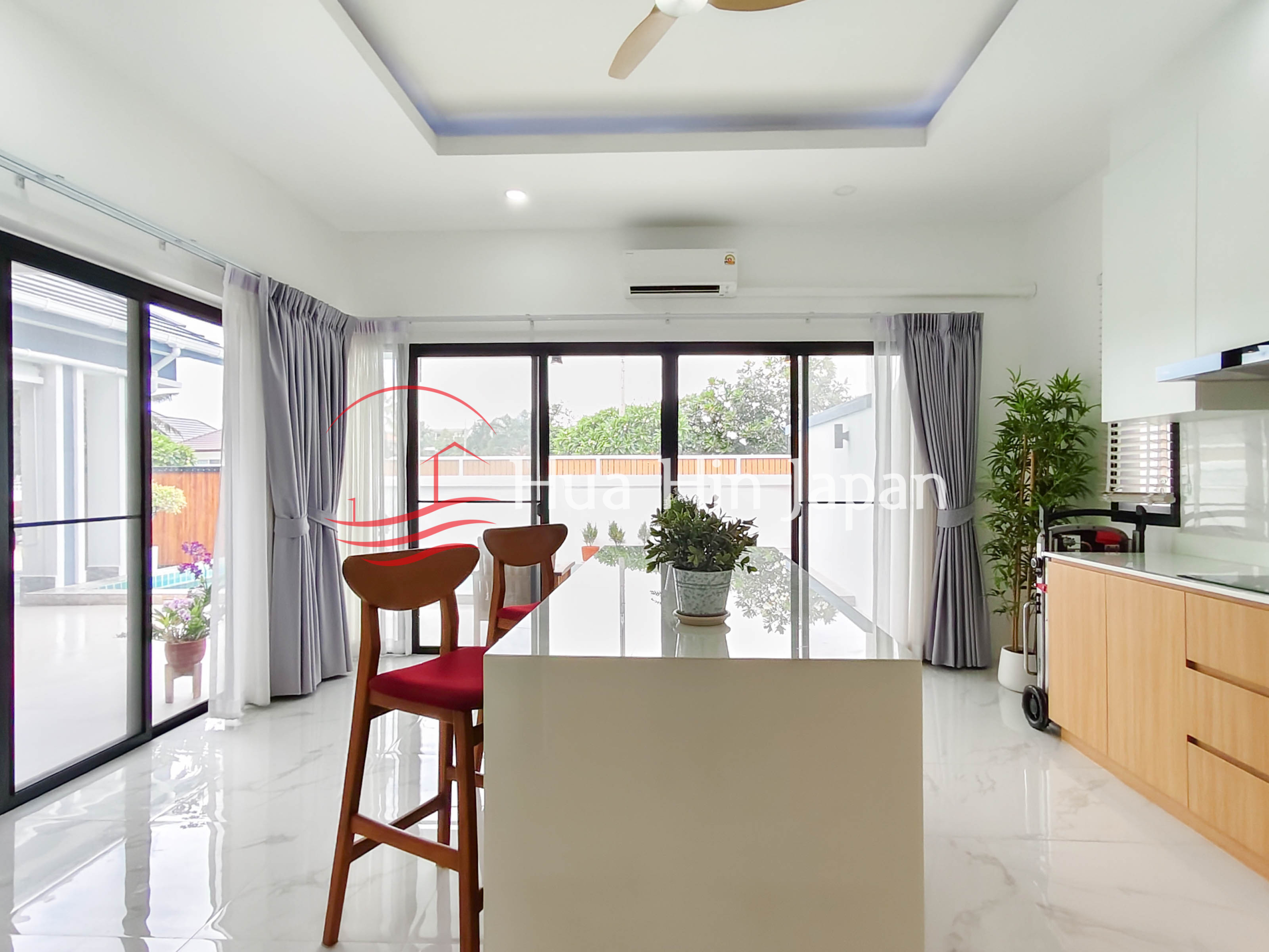 Modern living room with sofa, dining table, large glass doors, curtains, and indoor plants