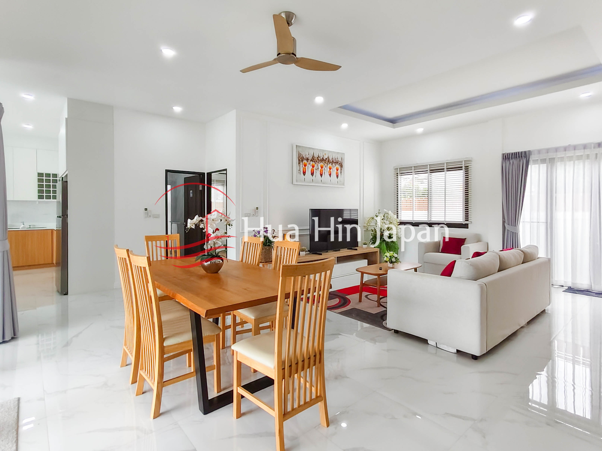 Bright modern dining room with wooden table, chairs, sofa, ceiling fan, and wall artwork