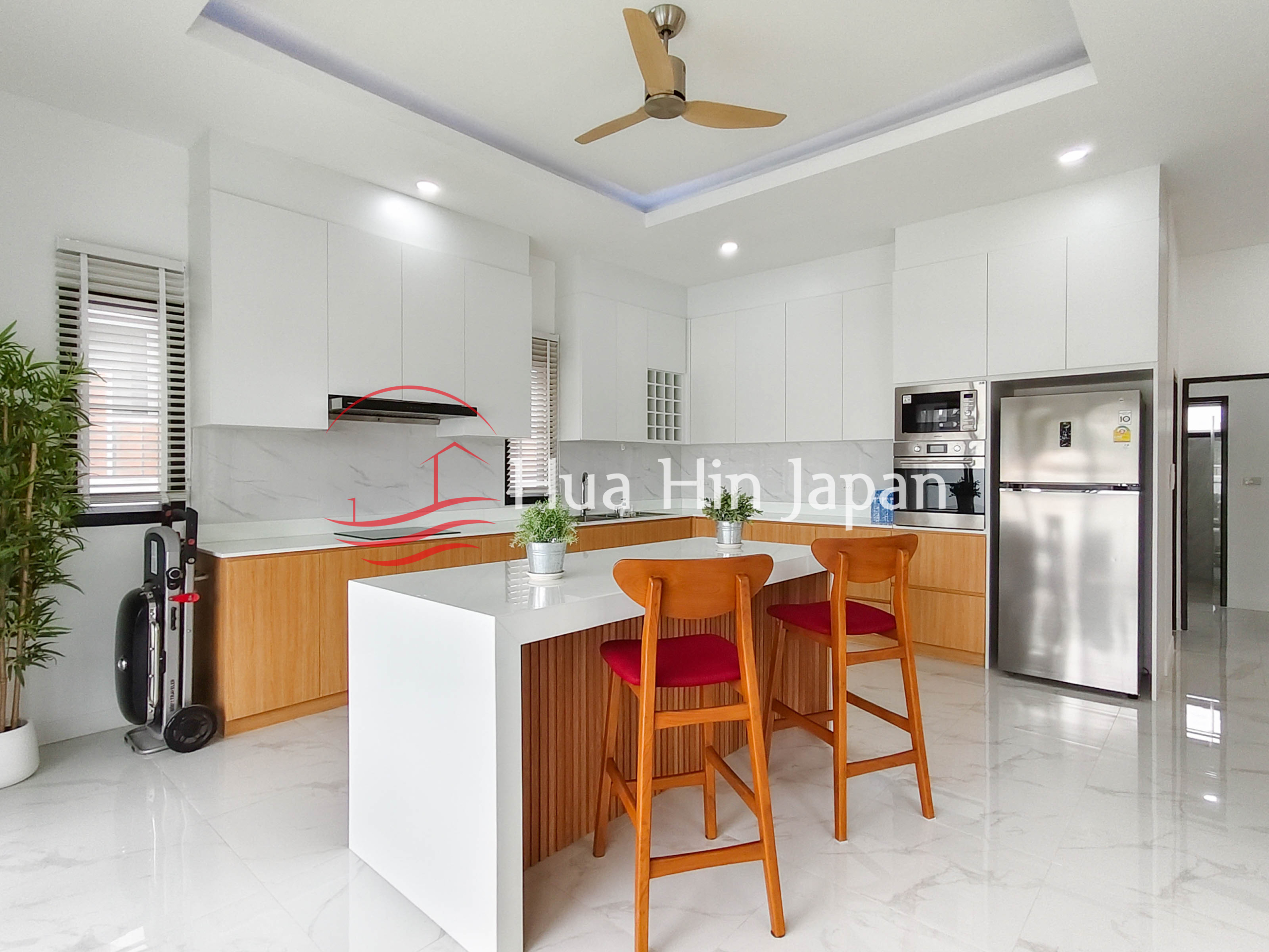 Modern dining and kitchen area with wooden table, chairs, ceiling fan, and white cabinets