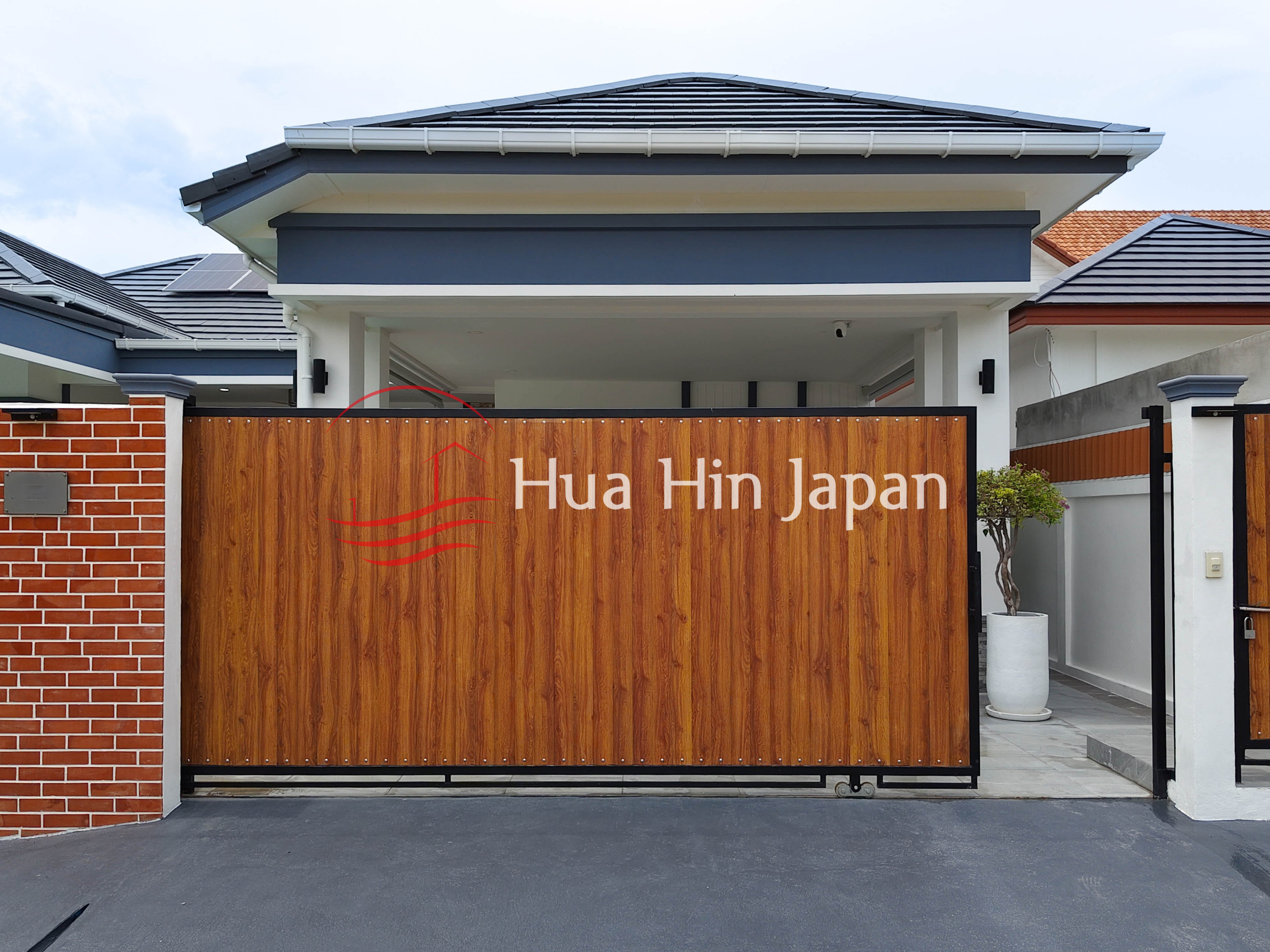 Modern villa exterior with covered entrance, gray tiled roof, and wooden gate